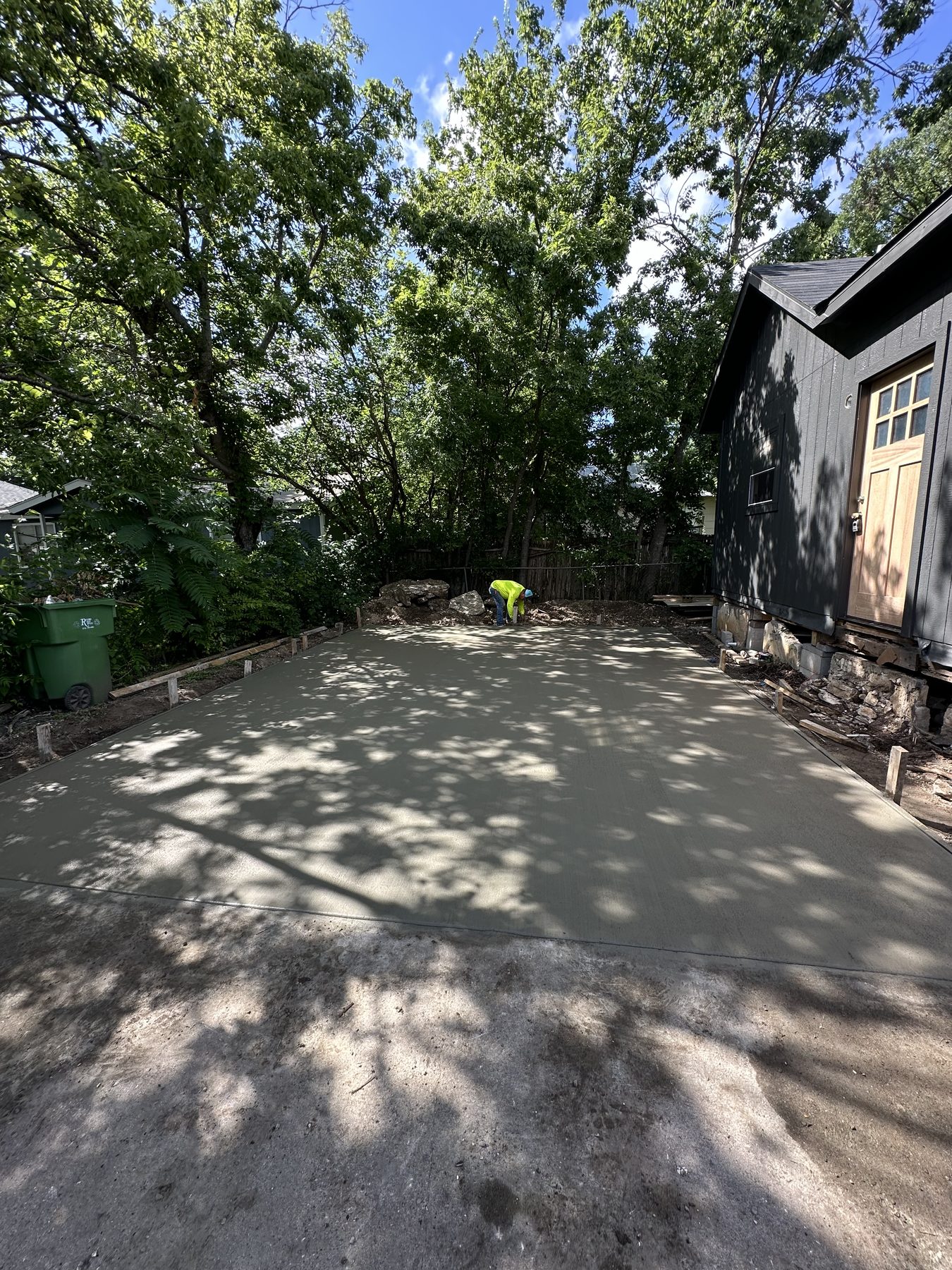 Back patio slab poured behind a dark-sided house under oak trees
