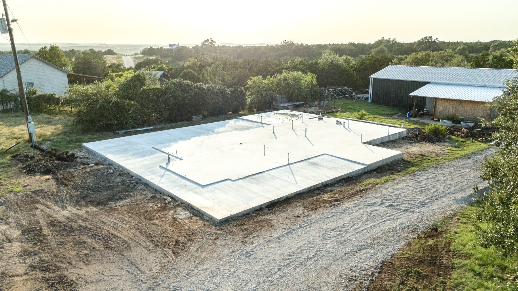Aerial view of a freshly poured slab foundation beside a metal shop building